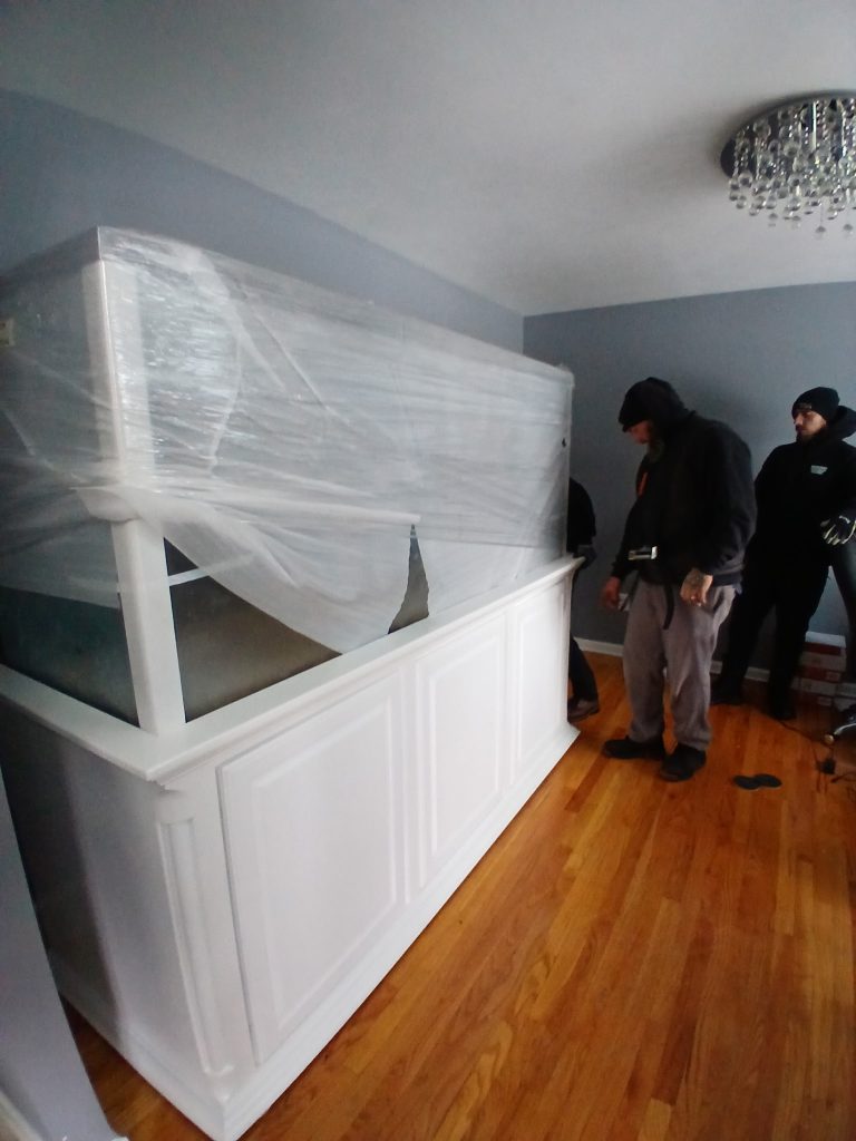 Reliable Movers crew carrying a 1,200-pound saltwater fish tank into a home in Liverpool, NY on December 8, 2025.